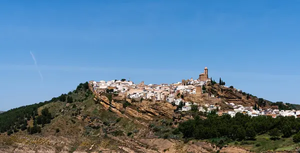 stock image a Spanish hilltop village, its white buildings crowned with a church, perched atop a rugged hill, under the vast expanse of a clear blue sky.