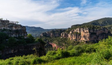 Majestic cliffs rise like ancient citadels, crowned with verdant forest, standing guard over the valley's lush carpet of trees under a serene sky. clipart