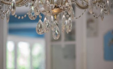 Zarif kristal damlalar lüks bir avizeye asılır. Mavi ve beyaz aksanlı parlak bir iç mekan boyunca yumuşak bir ışık yansıtır. Huzurlu ve rafine bir atmosfer yaratır..