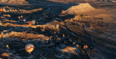 At dawn, hot air balloons float over a sprawling valley shadowed by undulating mountains, their colors vivid against the fading night. Below, patchwork fields and distant towns. clipart