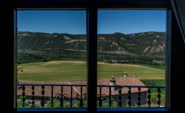 a picturesque view through an open window, framing the undulating golden fields and distant mountains, capturing the essence of a serene rural landscape clipart