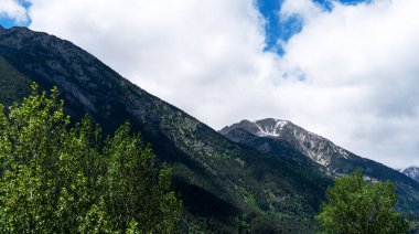 striking, majestic mountain peaks, still dusted with snow, towering above lush green forests under a dynamic sky dotted with clouds, capturing the grandeur of a mountainous landscape clipart