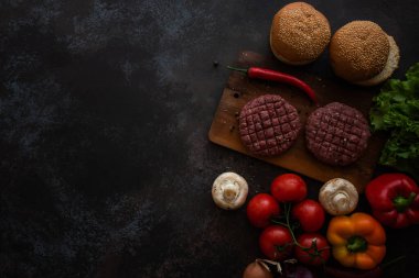 Fast food. Ev yapımı sulu burger yapmak için gerekli malzemeler. Üst ve düz siyah bir masada yatıyordu. Çiğ et, baharat, çörek, marul ve taze sebze..