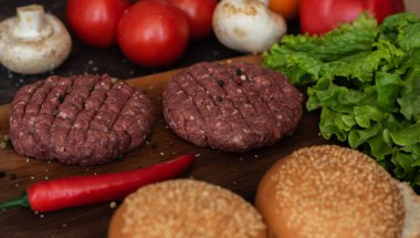 Taze doğranmış çiftlik hayvanları, siyah arka planda baharat, ot ve sebzelerle eski bir kesim tahtasının üzerinde sığır burger kızartıyorlar..