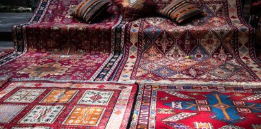 Karmaşık geometrik desenli renkli el dokuması halılar yere yayılmış ve yanında çizgili yastıklar var. Zengin renkleri, geleneksel zanaatkarlığın canlı bir gösterisini yaratıyor..