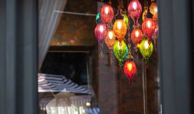 vibrant multicolored glass lanterns with intricate metal details hang in a cozy, dimly lit interior, creating a warm ambiance. Reflection in the background reveals striped fabric and a framed mirror clipart