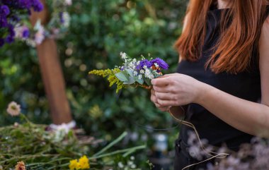 Beyaz papatyalı, kırmızı saçlı bir kadının tuttuğu mor ve turuncu çiçekli narin bir buket bulanık yeşil arka planda. Taze, doğal ve yaz havası..