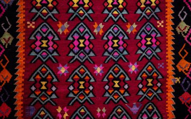 Kırmızı, turuncu, sarı, pembe ve siyah renkli karmaşık geometrik desenli geleneksel halı. Simetrik şekiller ve canlı renkler kalın ve zıt kenarlarla çevrili zengin bir duvar halısı tasarımı oluşturur..