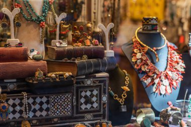 Türk mücevher ve biblolarının zarif bir gösterisi, deri kaplı kitaplarla çevrili ve İstanbul 'un pazar yerindeki hazinelerinin zengin duvar halısını gözler önüne seren işlemeli ahşap bir kutunun üzerinde duruyor..