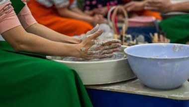 A person wearing a green apron with hands covered in clay is shaping a piece of pottery on a spinning wheel. Fully engaged in the creative process with a focus on the clay piece. clipart