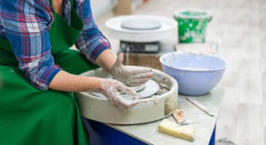 Seramik oluşum sürecine odaklanarak dönen bir çömlek çarkının üzerindeki ıslak çamuru şekillendiren eller. Sanatçının elleri kille kaplı, çömlek yapımının dokunsal ve yaratıcı doğasını gösteriyor..