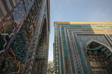 Özbekistan 'daki güneş ışığıyla aydınlanmış mezarlık cepheleri, alçak bir açıdan çekilmiş. Geleneksel İslami süslemeleri vurgulayarak, mozolenin duvarlarını entrika ciltli turkuaz ve kobalt fayanslar kaplıyor.