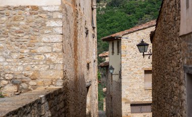 Antika bir köydeki antik taş binalar arasındaki dar bir ara sokak yemyeşil bir yamaca çıkıyor. Kırsal cazibe eski sokak lambaları ve geleneksel mimariyle vurgulanır.