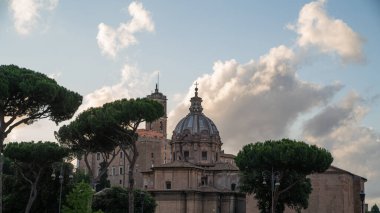 Barok kilise kubbesi ve antik Roma çan kulesi Roma, İtalya 'da yumuşak akşam ışığı altında şemsiye çam kulesinin arkasında yükseliyor. Roma Forumu yakınlarındaki tarihi binalar yemyeşil ve dramatik gökyüzü ile harmanlanır.