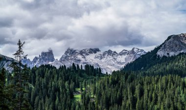 Bereketli yeşil vadisi olan sakin bir dağ manzarası. Karla kaplanmış tepeler arasında, kısmen puslu bulutlarla kaplanmış, dramatik bulutlu gökyüzüne karşı.