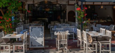 Canlı kırmızı çiçekler ve yeşilliklerle süslenmiş beyaz sandalyeleri ve masaları olan büyüleyici bir açık hava kafesi. Davetkar ortam, sakin bir yemek ya da kahveden zevk almak için mükemmel..