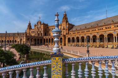 Sevilla 'daki Plaza İspanya' da güzel dekore edilmiş mavi ve beyaz seramik bir balustrade, plazanın karmaşık Rönesans mimarisi ve arka planda yansıtıcı bir kanal.