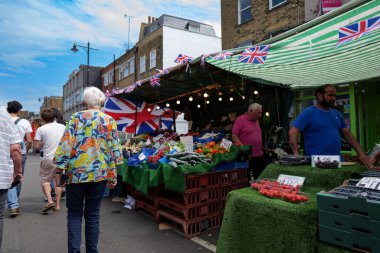 Londra - 06 03 2022: Bayan, Chapel Market 'te meyve ve sebze tezgahının önünde yürüyor