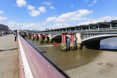 Londra - 06 10 2022: Kız Blackfriars Köprüsü 'nde cep telefonuna bakıyor ve Blackfriars Demiryolu Köprüsü' nün altında bir turist sandalına biniyor..