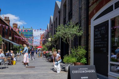 Londra - 06: 20 2022 Bir kadın, Chelsea 'deki Pavilion Bulvarı' nda bir kafede insanların oturduğu bir poşeti almak için eğildi.