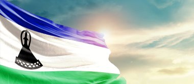 Lesotho waving flag in beautiful sky with sun