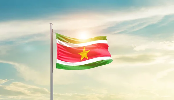 stock image Suriname waving flag in beautiful sky with sun