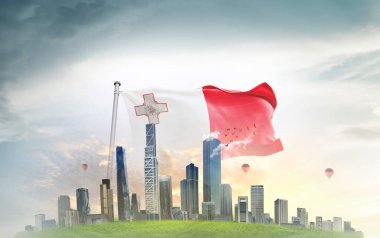 Malta ulusal bayrağı gökyüzünde dalgalanırken, arka planda büyük megapolis şehir binaları  