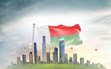 Madagaskar ulusal bayrağı gökyüzünde dalgalanan bulutlar, arka planda büyük megapolis şehir binaları  