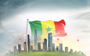 Senegal ulusal bayrağı gökyüzüne doğru sallanıyor. Arka planda büyük şehir mimarisi var. 