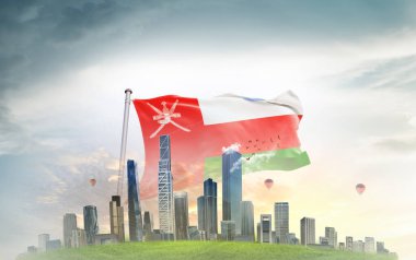 Umman ulusal bayrağı gökyüzünde dalgalanırken bulutlar, arka planda büyük şehir mimarisi 