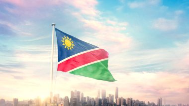 Namibya bayrağı mavi gökyüzü arka planında şehir manzarası ile dalgalanıyor 