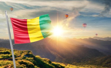 Gün batımında bayrak sallayan Gine Dağlarda arka planda sıcak hava balonları