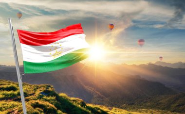 Tacikistan günbatımında bayrak sallıyor ve arka planda sıcak hava balonları var.