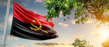 Angola ulusal bayrağı ağacın yanındaki bulutlara karşı dalgalanıyor