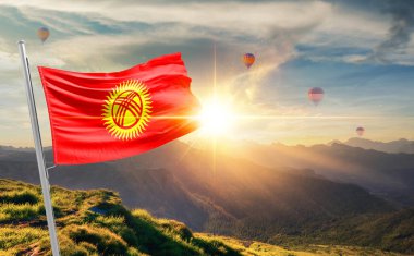 Kırgızistan günbatımında bayrak sallıyor. Arka planda sıcak hava balonlarıyla dağlarda.