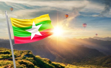 Dağlarda gün batımında dalgalanan Myanmar bayrağı, arka planda sıcak hava balonları 