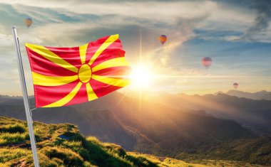Kuzey Makedonya bayrağı dağlarda gün batımında dalgalanırken, arka planda sıcak hava balonları 