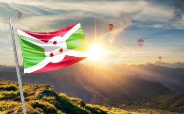 Burundi bayrağı dağlarda gün batımında sallanıyor, arka planda sıcak hava balonları. 