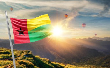 Dağlarda gün batımında sallanan Gine-Bissau bayrağı, arka planda sıcak hava balonları 
