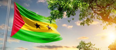 Sao Tome ve Principe gün batımına karşı ağacın yanında bayrak sallıyorlar.
