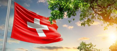 İsviçre gün batımına karşı ağacın yanında bayrak sallıyor