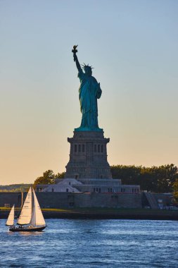 Gün batımında New York 'ta Özgürlük Heykeli' nin yanından geçen küçük yelkenli resmi yumuşak gün batımında