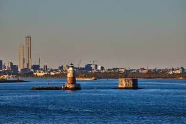 Görüntü: Robbins Resifi Deniz feneri New York 'ta, arkasında altın ışıklı ve endüstriyel şehir