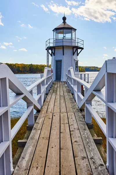 Image of Wood boardwalk with white railing leading to small Maine lighthouse