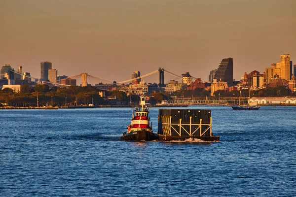 Image of Small industrial ship pulling shipping containers from side in industrial New York City golden hour