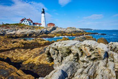 Maine 'in kayalık kıyılarına bakan taşlaşmış ahşap gibi kayalara odaklı beyaz deniz feneri görüntüsü