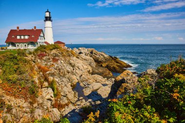 Maine 'deki klasik beyaz deniz fenerinin görüntüsü kayalık sahillerdeki okyanusa bakıyor.