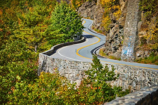 Image of Detail zoom on road with stone wall winding through forest along cliffs