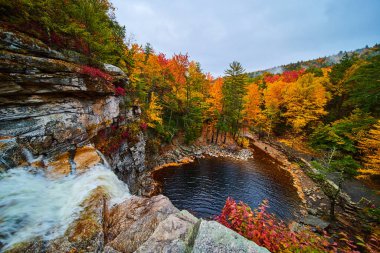 Nehrin kenarına düşen şelale görüntüsü ve çarpıcı sonbahar renkleriyle çevrili.