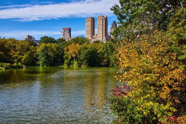 New York 'un arkasında yüksek binalar bulunan Central Park' ın içindeki göl ve ormanların görüntüsü